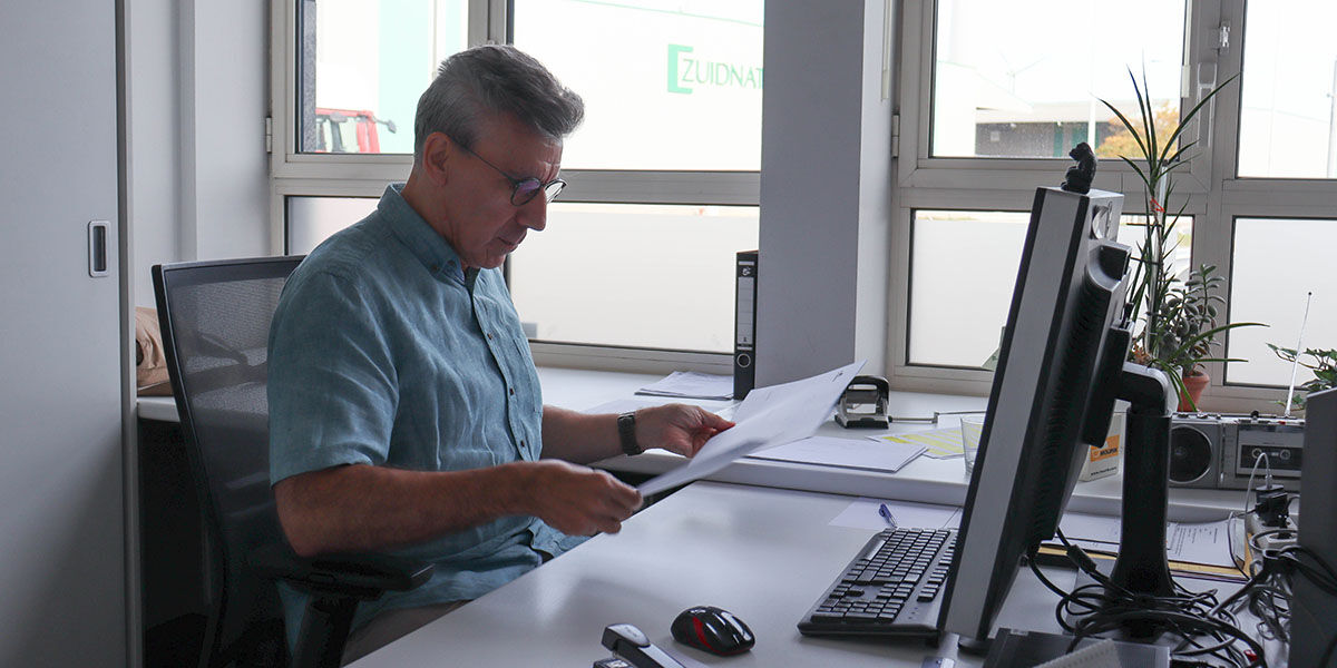 Collega Rudi aan het werk achter zijn computer met papieren in zijn hand